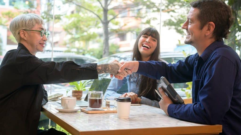 A group of people smiling and shaking hands at a café table.