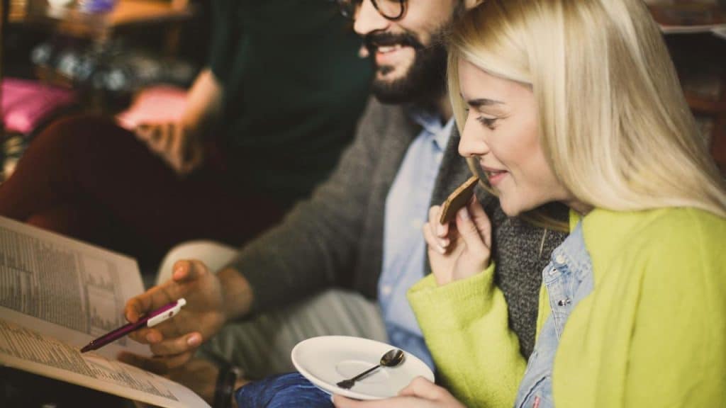 A couple sitting closely while reading a menu and sharing a dessert in a cozy café.