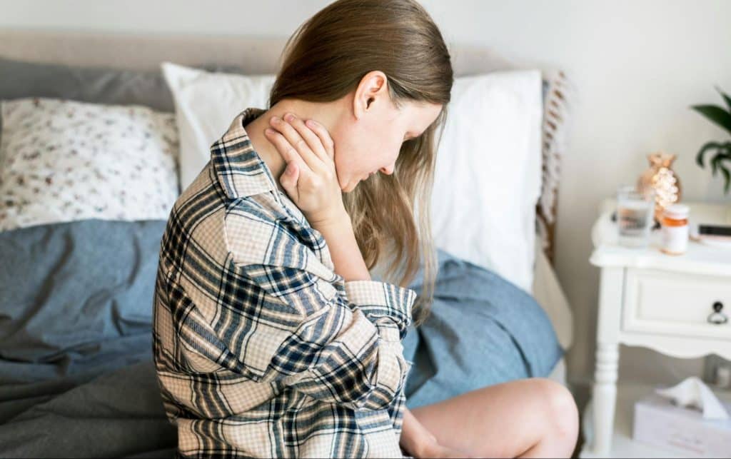 A woman sitting at the bed and holding her neck