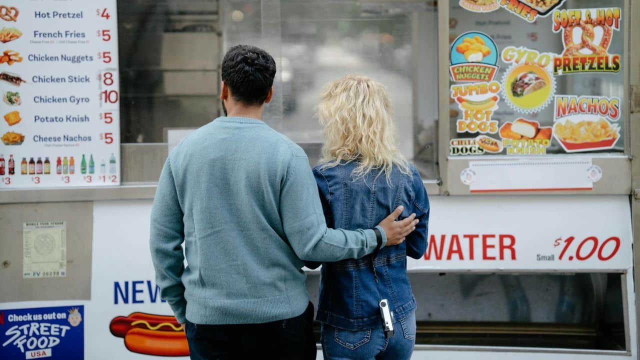 A man and woman stand with their backs turned looking at a street food menu.