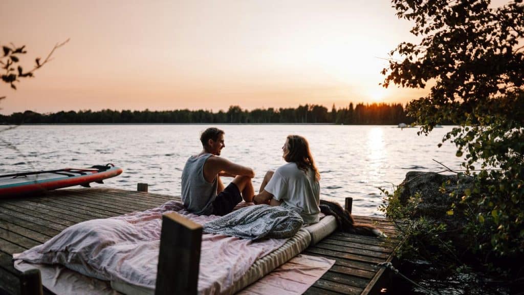 A couple sitting on a dock by a lake, watching the sunset together.