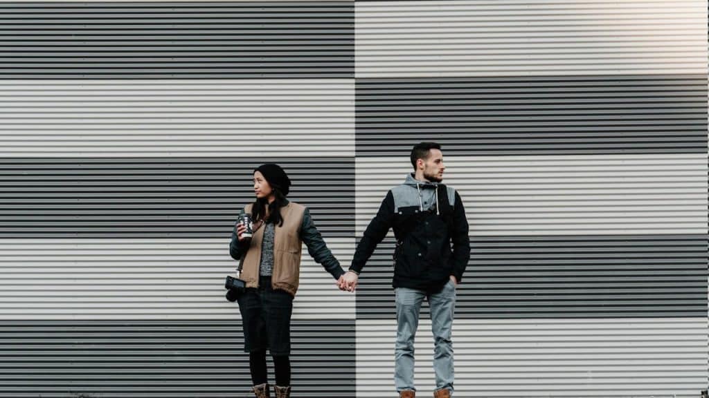 A man and woman looking away while holding each other's hands.