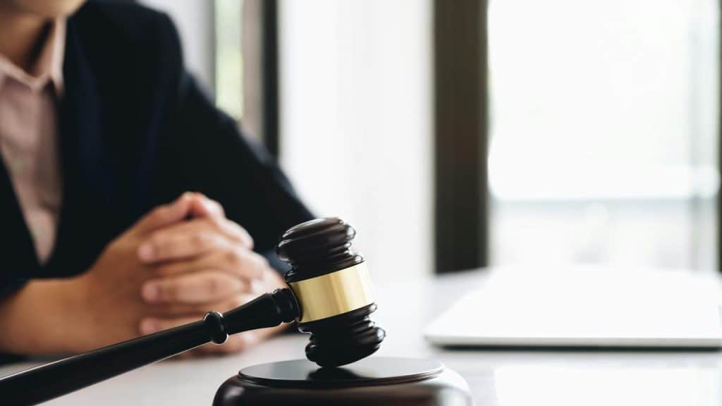 A judge’s gavel on a desk with a person sitting in the background.
