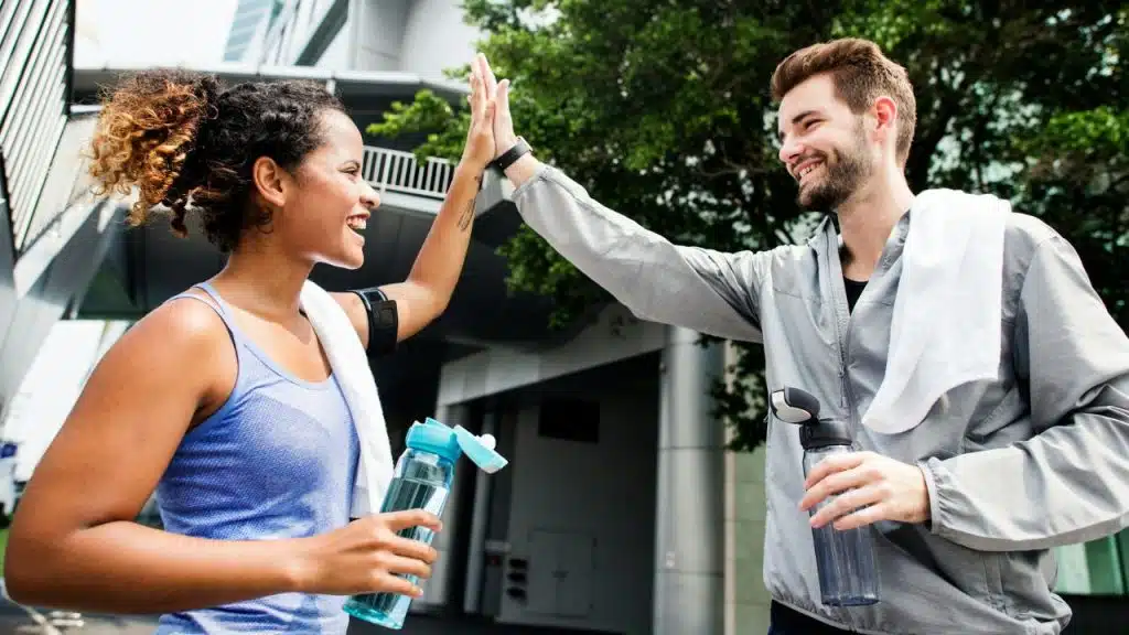 A man and woman in athletic wear give each other a high-five outdoors.