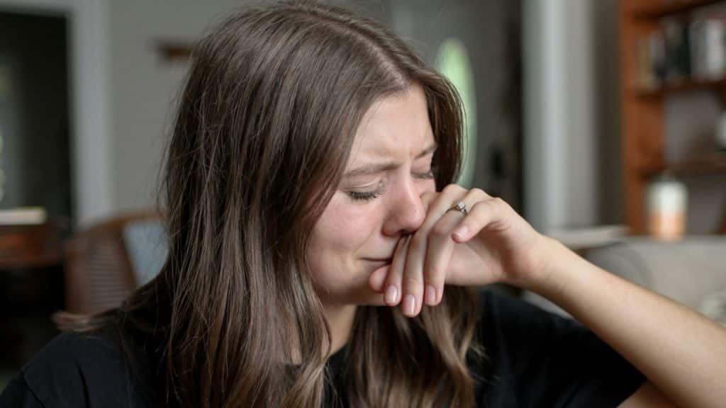A woman with long hair rests her hand against her face while looking down with eyes closed.