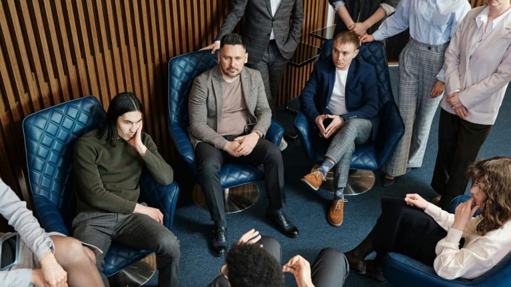 A group of people sit in blue chairs arranged in a circle for a discussion.
