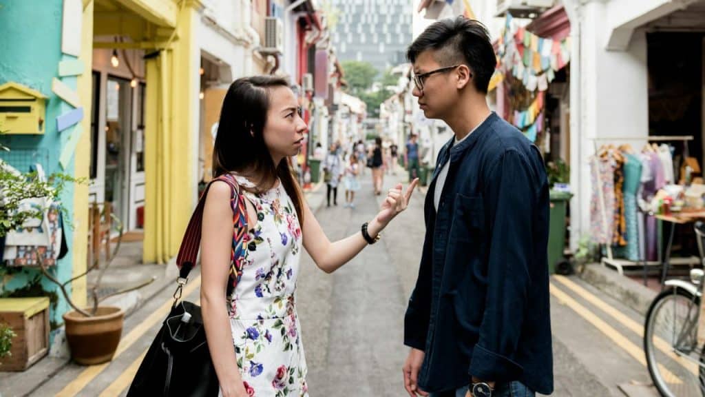 A woman points a finger at a man while standing on a crowded city street.