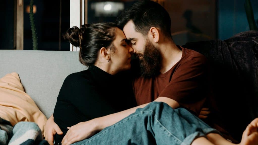 A man and woman sitting on a couch kissing.