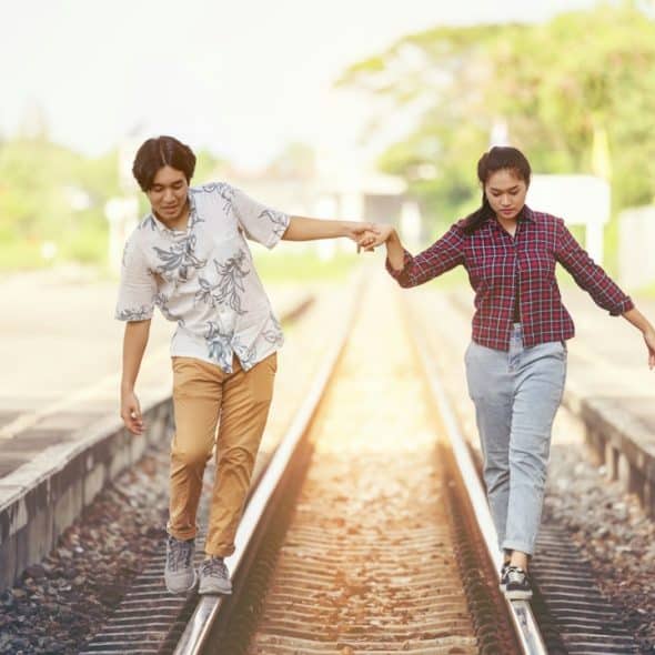 A couple holding hands and walking on railway tracks at a railway station.