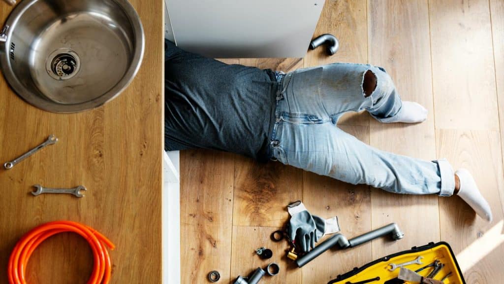 A man fixing a plumbing leak in the kitchen.