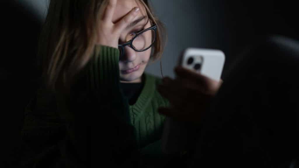 A person wearing glasses looking stressed while using a smartphone.