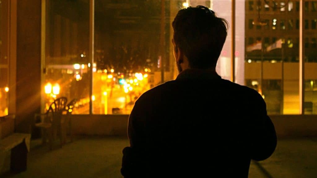 A man's silhouette is seen from behind as he looks out at a city at night.
