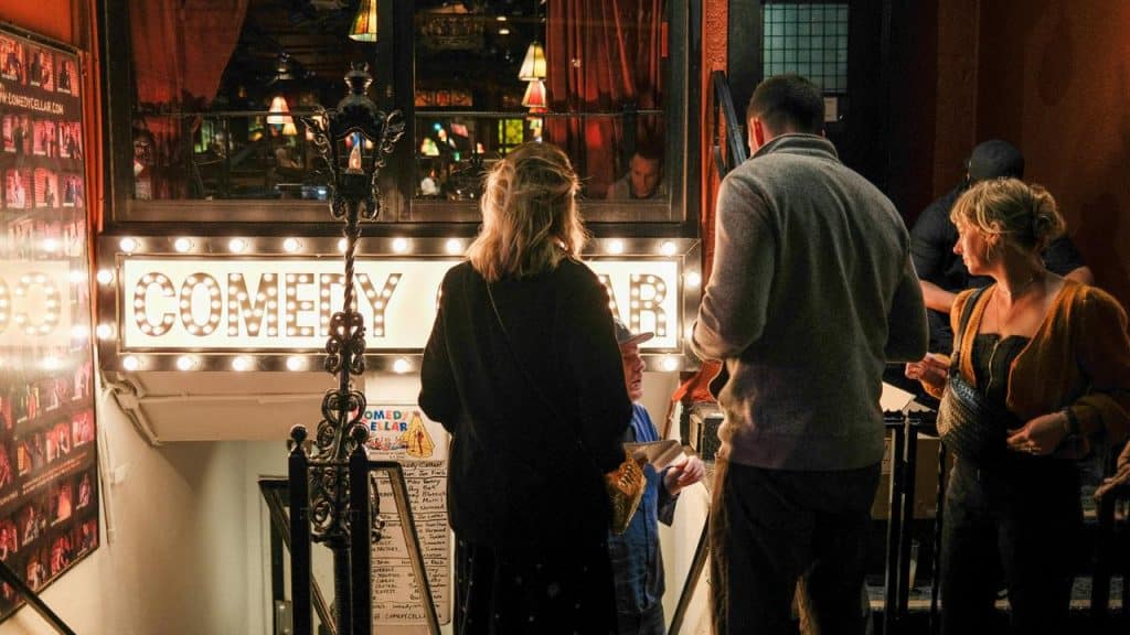 A group of people entering a comedy club at night.