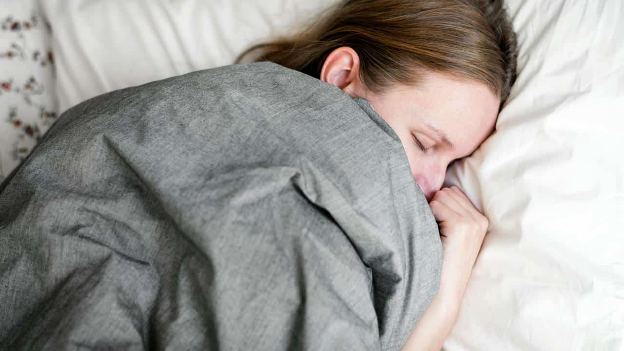 A woman sleeping under a gray blanket.