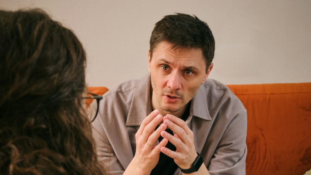A man with his hands raised speaks to a woman with long, curly hair.