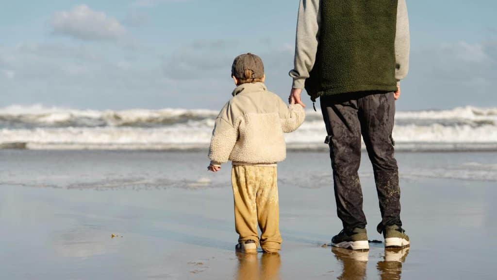 A child and adult holding hands on a beach shore.
