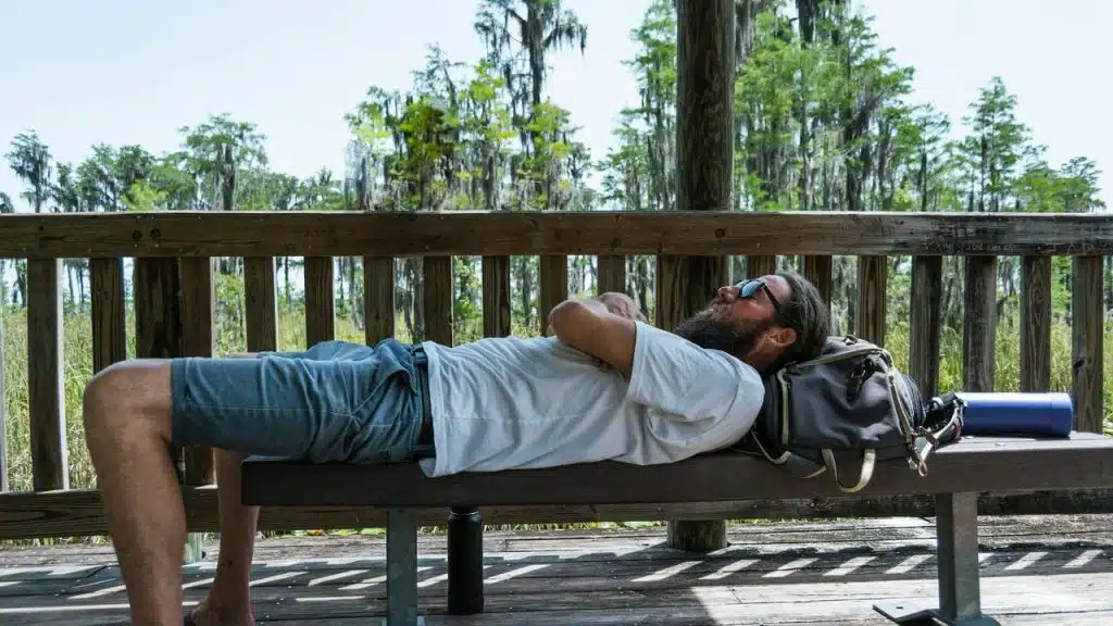 A man resting on a bench outdoors with trees in the background.
