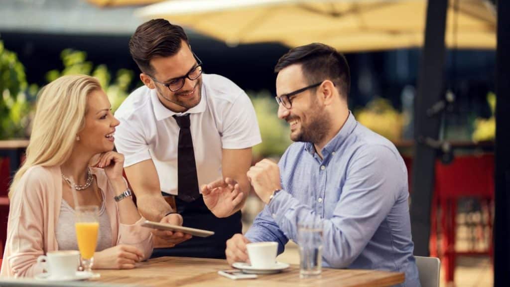 A server shows a digital tablet to a smiling man and woman at a table.