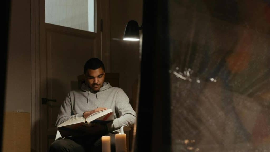 A man reading a book by candlelight indoors.