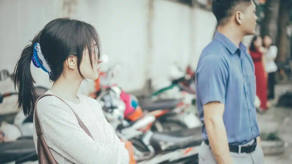 A woman with dark hair tied back looks sideways while standing near a man.