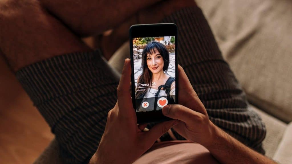 A person holding a phone showing a dating app profile on the screen.