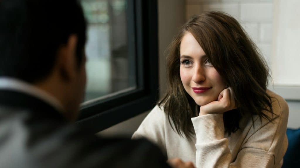 A woman rests her chin on her hand while looking warmly at a man.