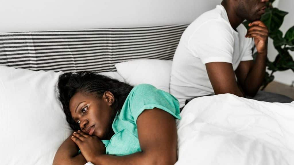 A woman in a green shirt lies in bed, looking away from a man.