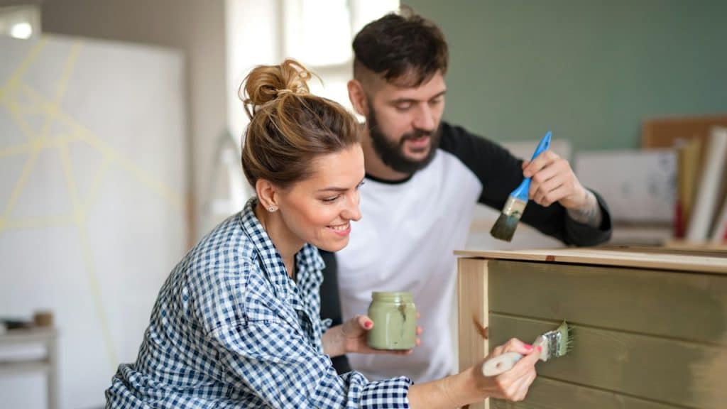 Happy couple painting furniture indoors at home relocation.