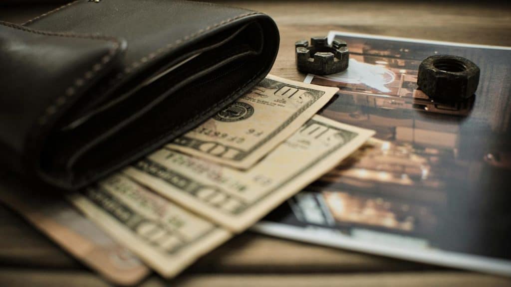 A leather wallet with cash partially visible on a table beside a photograph.