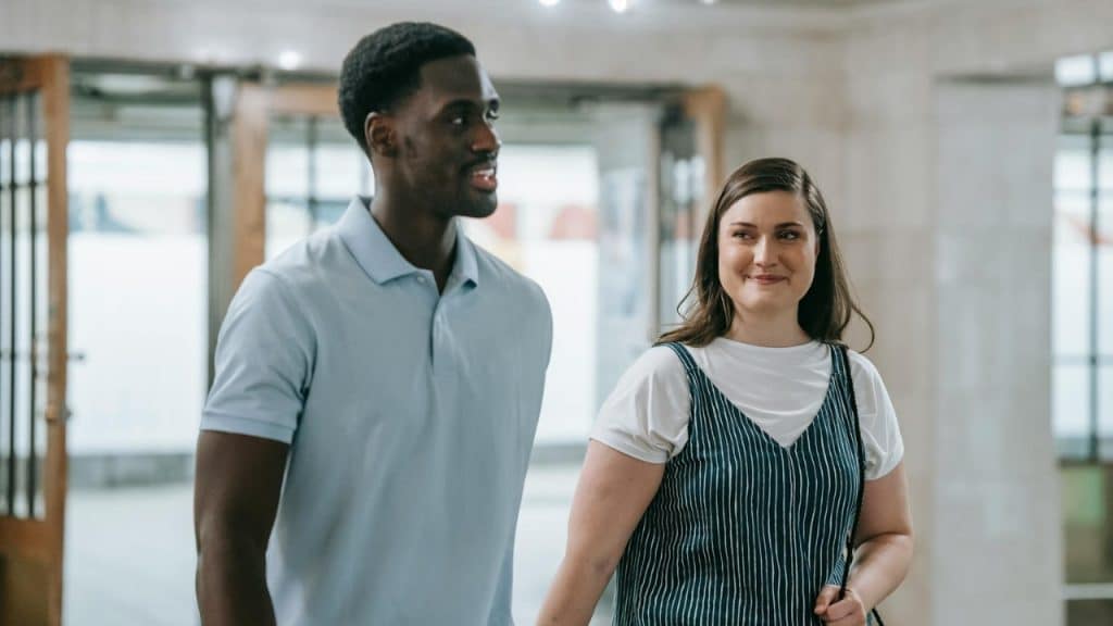 A man in a polo shirt and a woman in a jumper walk together and smile.