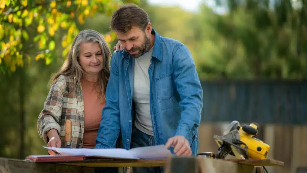 A couple reviewing plans together outdoors near a workbench.