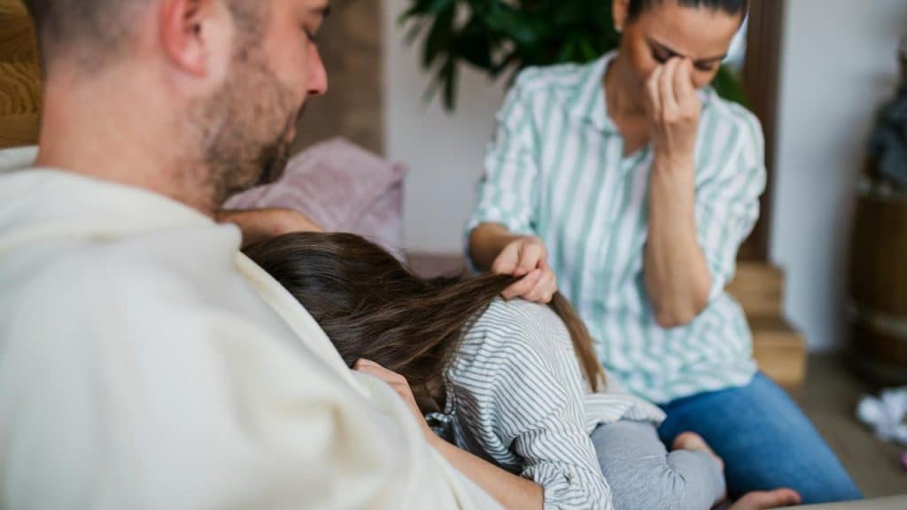 A father comforting a crying child while the mother sits upset.