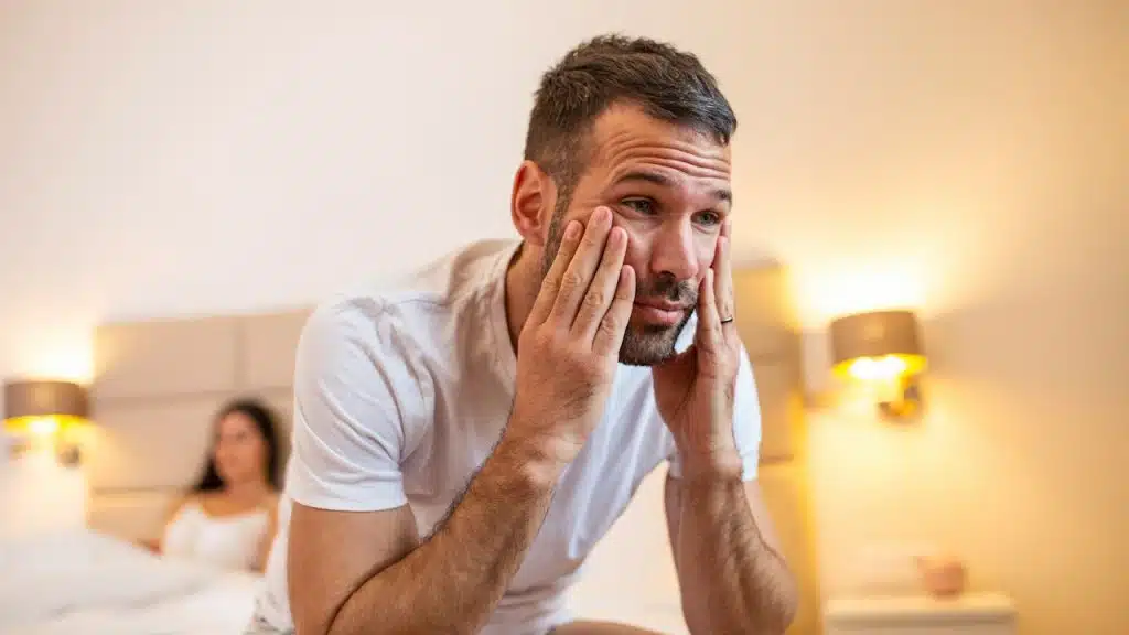 A woman in lingerie is sitting on the bed while her sad, frustrated man is thinking about relationship problems.