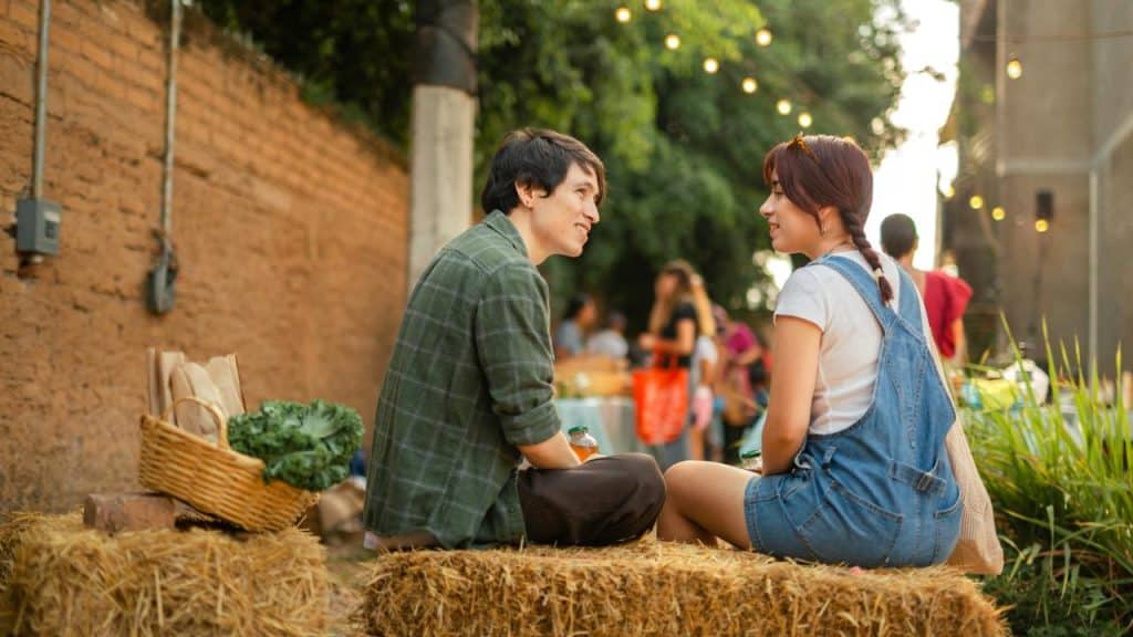 A young couple sitting on hay bales outdoors, talking at a casual evening gathering.