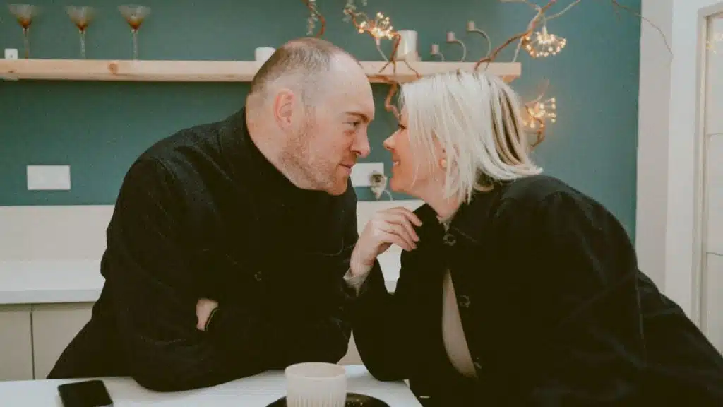 A man and woman lean toward each other across a table, making close eye contact.