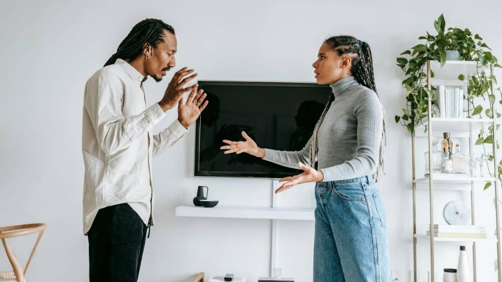 A man and woman with braided hair stand facing each other, gesturing with their hands.