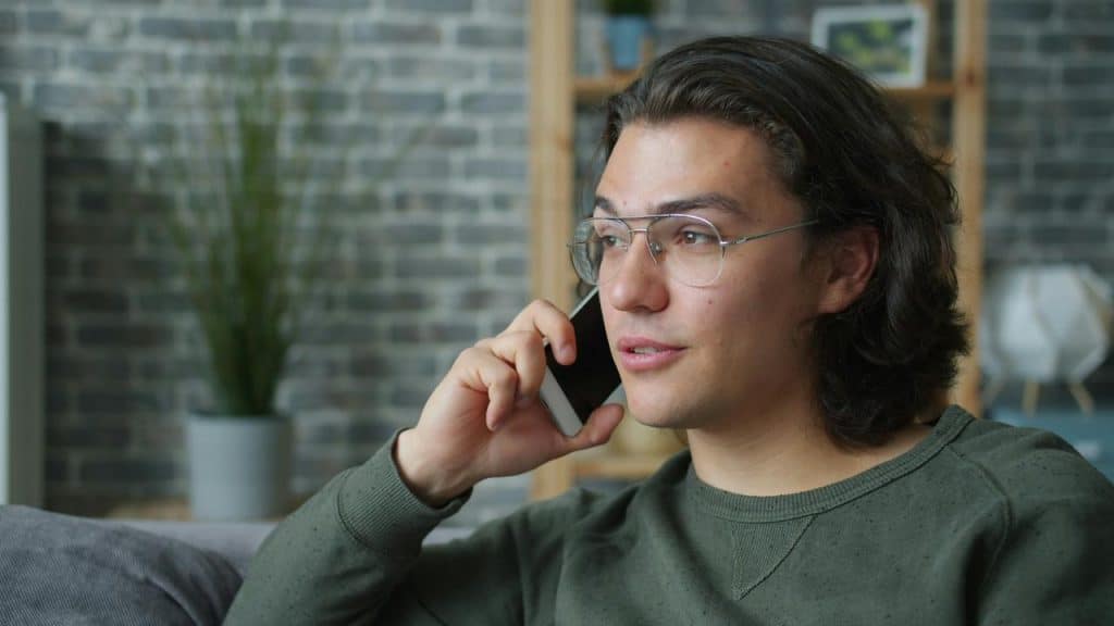 A young man wearing glasses talking on his phone in a modern office or co-working space.