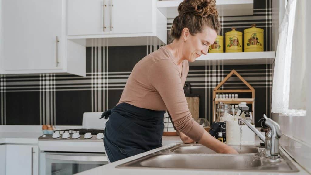 A woman washing dishes at a kitchen sink in a bright home.