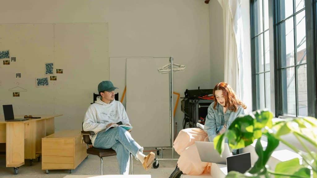 A man and a woman working on laptops in a bright, minimalist studio.