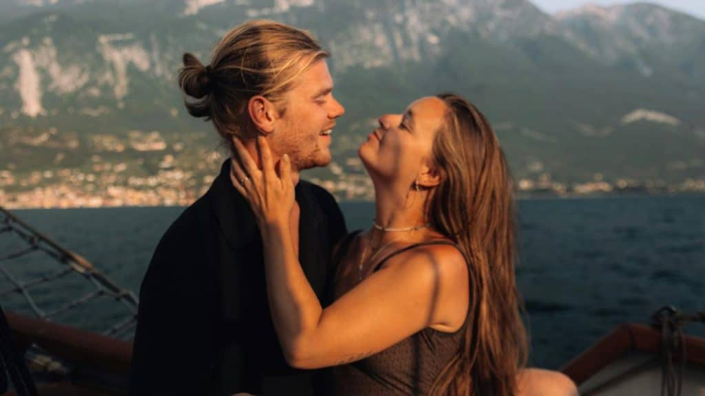 A couple embracing on a boat with mountains and water in the background at golden hour.