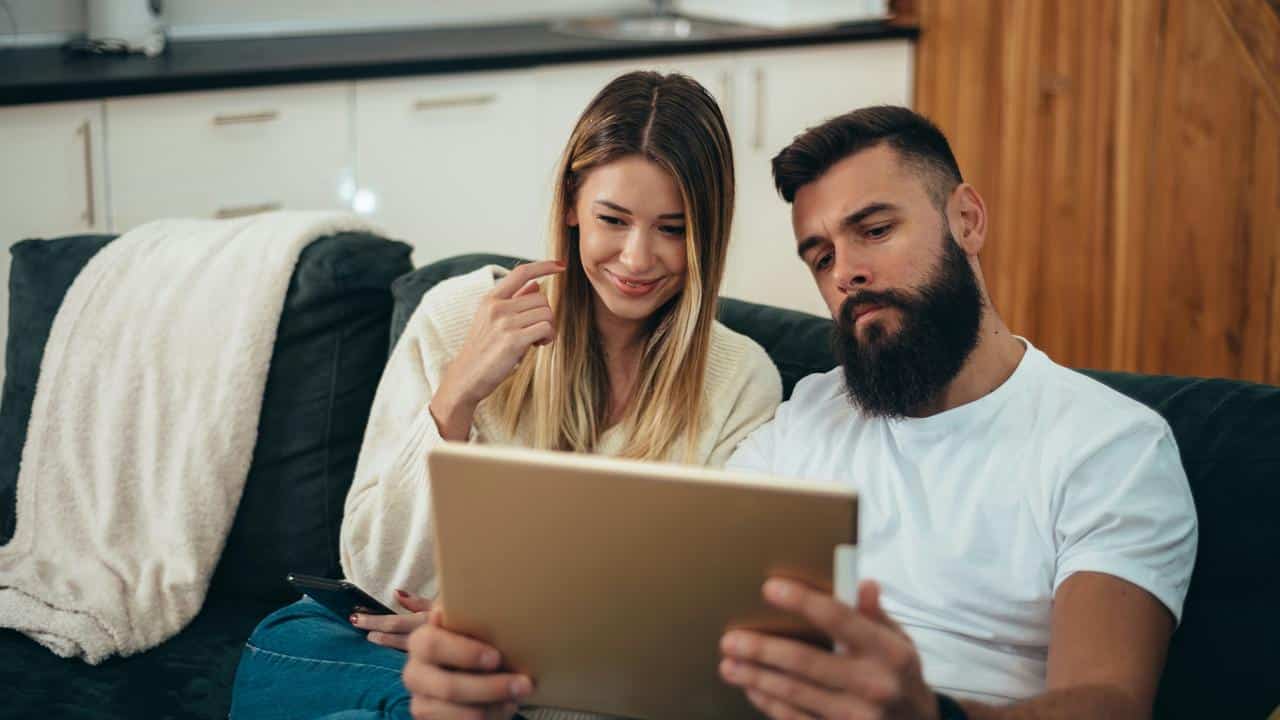 A couple sitting on a couch looking at a tablet.