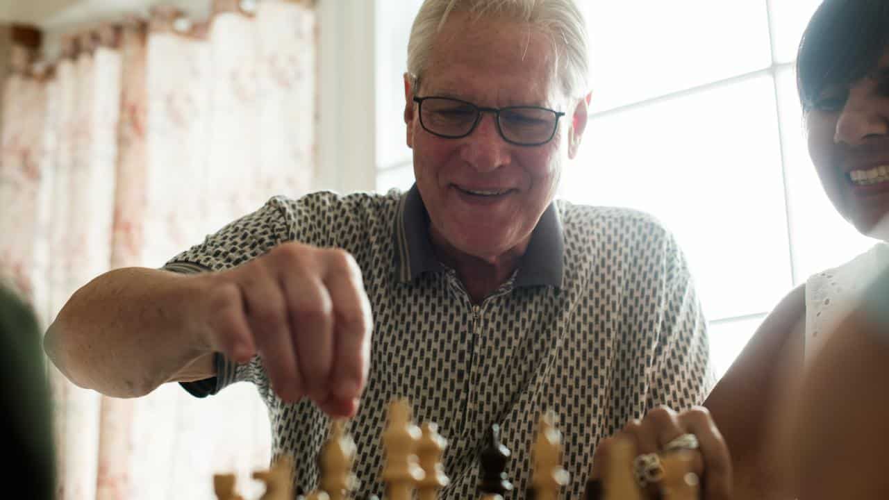 An elderly man moving a chess piece on a board.