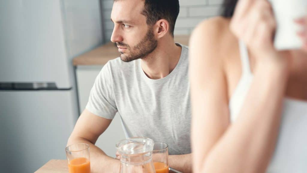 A man in a grey t-shirt sits at a table looking off to the side.
