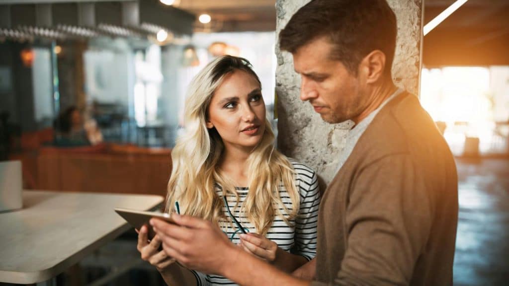 A man and woman discussing something on a tablet in a café.