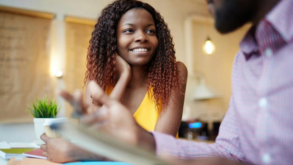 A woman smiling attentively while talking with someone at a café table.