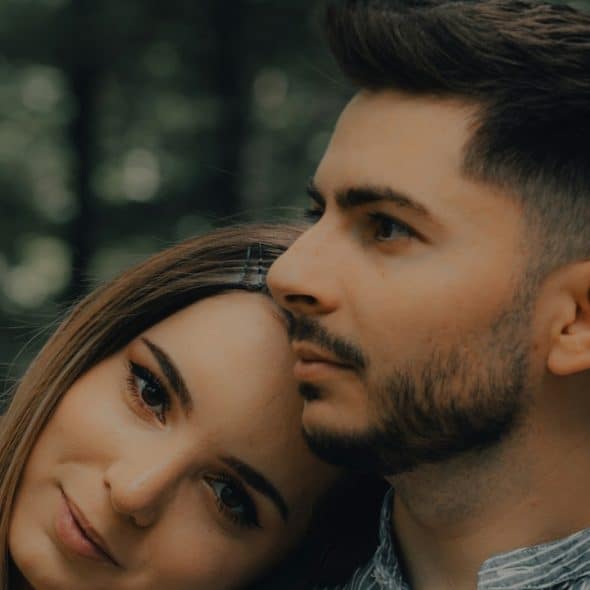 A woman resting her head on a bearded man’s shoulder.