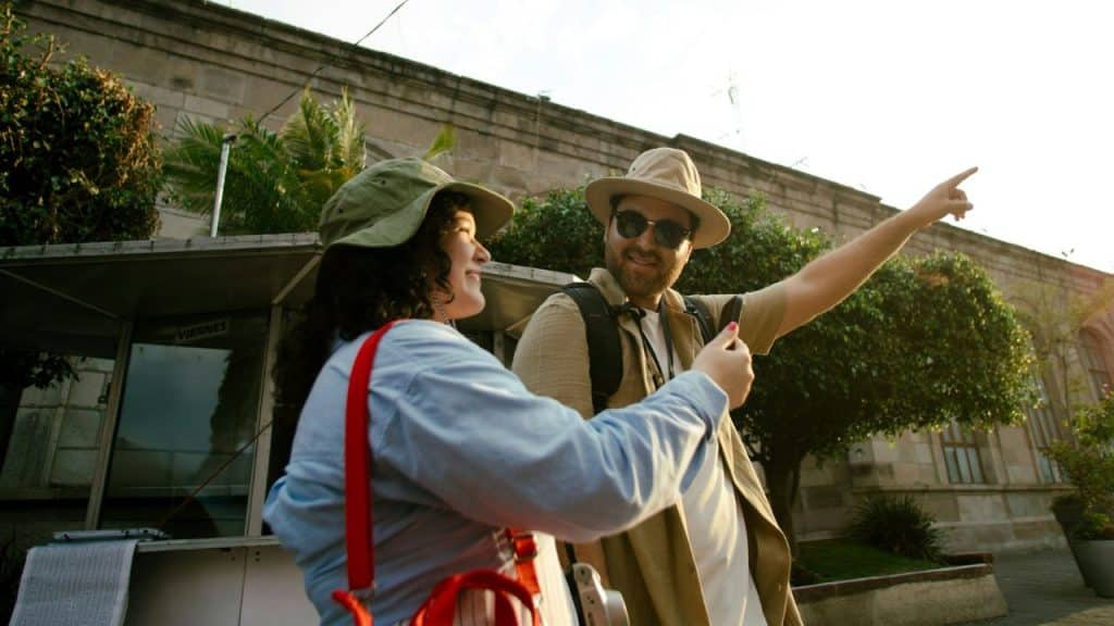 Two people in sun hats stand outdoors while the man points toward the distance.