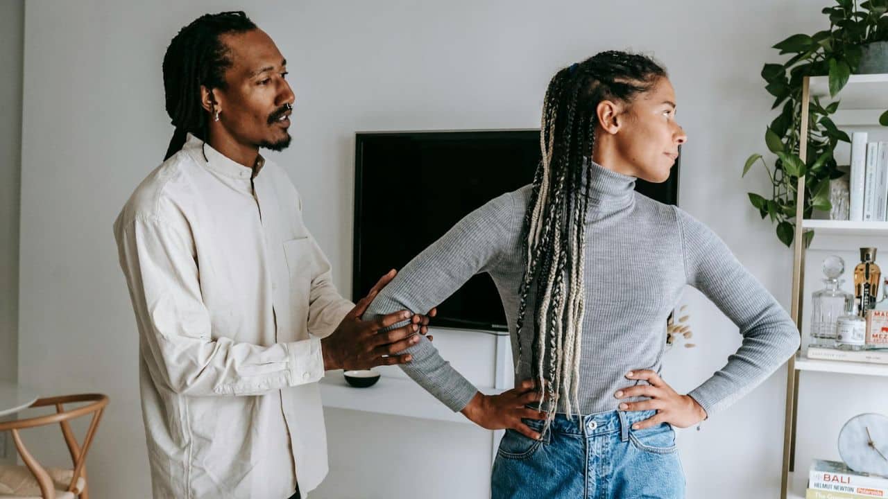 A man with dreadlocks touches the arm of a woman who is looking away from him.