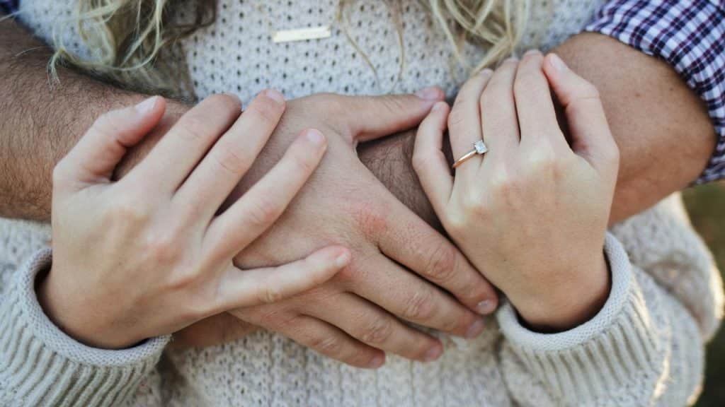 A close-up of a couple’s hands clasped together, showing an engagement ring.