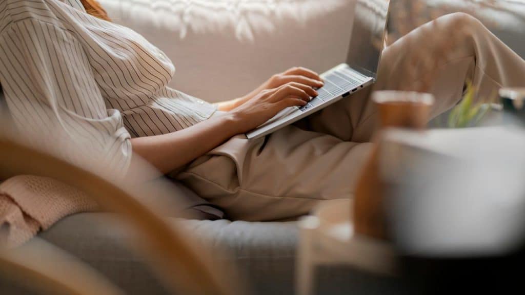 A person sitting comfortably and typing on a laptop in a cozy living space.